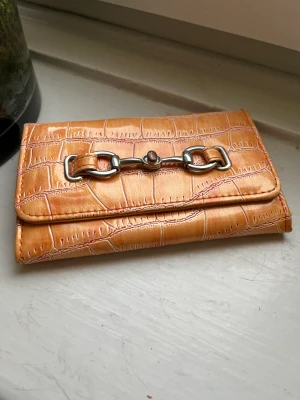 Plånbok  - En orange plånbok som jag inte var vart den kommer ifrån. Den har en silver ditalj där framm och har mönster.  Kommer sälja pga inte använder lika mycket som förut! 