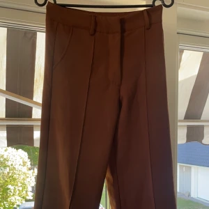 Bruna kostymbyxor från madlady - Säljer dessa supersköna högmidjade kostymbyxor från Madlady då de inte blivit använda och är för små i midjan.   Lite skavanker finns såsom att de är lite nopprig i benen men ingenting man tänker på. Notera att jag är 163 cm🤗 Storlek XS🩷