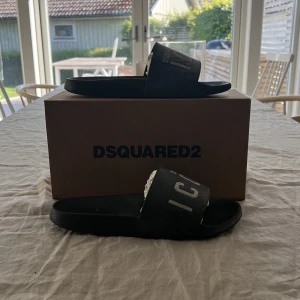 DSQUARED2 tofflor - Dags att sälja min omtyckta DSQUARED2 tofflor som är väldigt snygga och stilrena. Har använt dom i ungefär ett år nu så ganska använda, perfekt inför sommaren sol och bad. Köpta ifrån fartfetch för 1650kr, säljs inte längre. Fråga på:) MVH Albin 