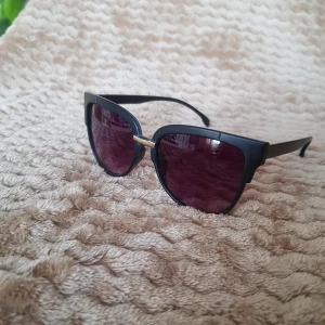 Solglasögon - Matta svarta solglasögon med guld detalj och svart/grå glas. Diskret cateye modell