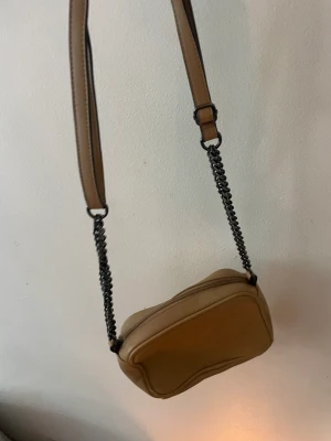 Liten beige axelremsväska  - Liten beige axelremsväska. Från Ulrika. Använd fåtal gånger. 