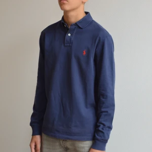 Långärmad Ralph Lauren piketröja - Långärmad Ralph Lauren piketröja i slim fit passform och marinblå färg. Tröjan är i bra skick, skriv vid eventuella frågor. **EGNA BILDER EJ FRÅN HEMSIDA!**