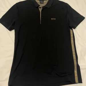 Hugo boss pike  - Hugo boss piké i svart/Guld Strl L I gott skick