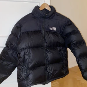 The North Face 1996 Retro Nuptse Jacka - Säljer en dunjacka från North Face i storlek L. Sparsamt använd så skicket är toppen. Jackan har även en tunn luva man kan fälla ut från kragen.