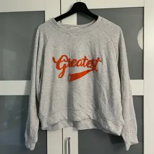Snygg grå sweatshirt/ långärmad från HM med ’Greatest’ skrivet på framsidan i cool orange färg. Texten ”står ut” från tröjan. Vintagevibbar!!  3 FÖR 2 på min sida!!