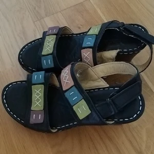 Sandal - Oanvänd sandal i  skinn. Reglerbar hälrem. 5 cm hög kilklack