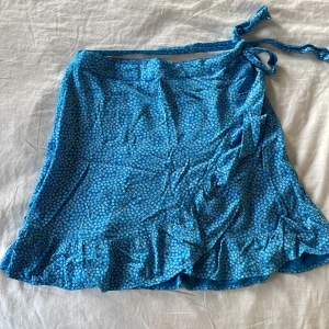 Omlottkjol - Blå med små vita blommor, stl S från Bikbok. Nypris 400 kr, endast använd fåtal gånger och inga defekter. Härlig ”tyngd” i tyget som gör att den faller snyggt.