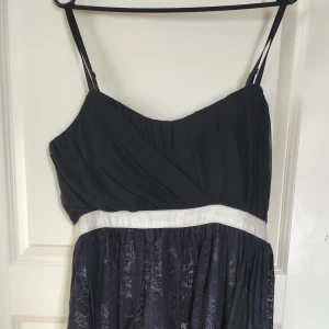 Svart klänning - Svartklänning med vitt under bysten och svart spets på underdelen med vit underkjol Emipre skyrning, oanvänd Kort där fram längre bak