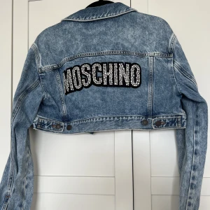 Cropped Denim Jacka - En äkta Moschino denim jacka som är cropped och utsmyckad på baksidan. Jättefin färg och passar till mycket. Använd endast 1 gång en kort stund, så den är så gott som ny i perfekt skick. Sista bilden är lånad. 
