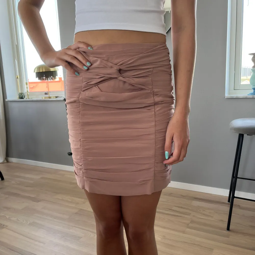 Draperad kort kjol i fin puderrosa färg stängs med dragkedja bak. Man kan ha den högt eller lågt i midjan.. Kjolar.