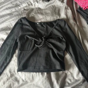 Svart ribbad topp med knytning - En svart ribbad topp med långa ärmar och knytning framtill. Toppen har en v-ringad hals och är croppad i modellen.