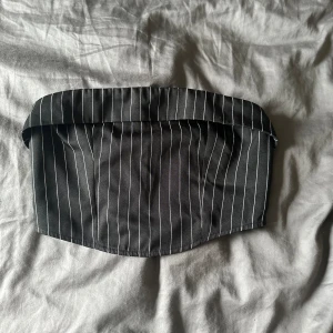 Svart randig tubtopp - En svart tubtopp med vita ränder. Toppen har en dragkedja på baksidan och en elastisk kant för bättre passform.