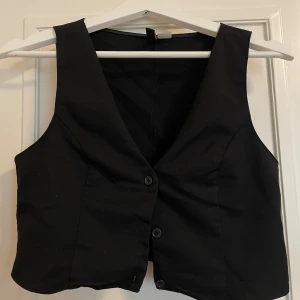 Svart väst från H&M - En svart väst från H&M i storlek S. Västen har en klassisk design med knappar framtill.