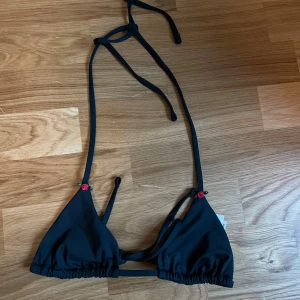 Svart bikiniöverdel från PINK - En svart bikiniöverdel från PINK by Victoria's Secret. Överdelen har knytband runt nacken och ryggen, vilket ger en justerbar passform. Den är tillverkad av 79% polyester och 21% elastan.