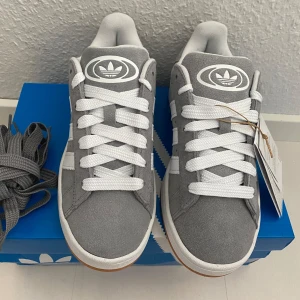 Nya grå Adidas Campus 00s 38 2/3 - Adidas Originals Campus 00 s j38 2/3 Gråa (Grey Three / Cloud White / Cloud White) Ingår både vita och gråa skosnören.  Nya och oanvända. Ligger kvar i kartong.  Köpta i svensk webbutik och kommer inte från någon massimport utomlands. 