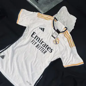 Real Madrid Hemmatröja 2023/2024  Säljer en ny Real Madrid hemmatröja för säsongen 2023/2024. Vit med guld- och mörkblå detaljer. Klubbmärke och Adidas