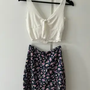 Vit Top (kan vara lite genomskinlig) och en blommig kjol med snitt på sidan.