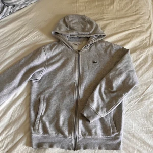 Lacoste Hoodie Zip Up - Hej! Jag säljer nu min Lacoste hoodie då den inte kommer till användning. Extremt skönt och perfekt för sommarkvällar ☀️. Snörerna saknas tyvär och de är ett ytterst litet hål i ryggen. Tveka inte att skicka ett pm ifall du har någon fråga  😊