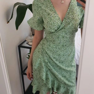 Grön sommarklänning intressekoll - Sommrig omlott klänning använd ett fåtal gånger, den är i ny skick utan fläckar och hål.🌷passar både xs och s. Säljer p.g.a att den inte kommit till användning. Jag är 165 cm och den slutar precis ovan knäna.