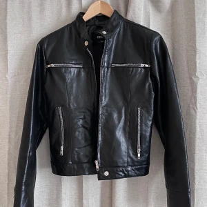 Skinnjacka biker mc - Superfin svart skinnjacka i bikerstil, 100% getskinn. Lika snygg öppen som stängd. I jättejättebra skick, mjuk för att vara skinn men bra kvalitet. Fickor i sidorna, krage och blixlåsdetaljer i ärmarna. Något markerade axlar. 