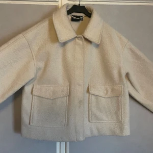 Kort kappa från vero moda  - En kort gräddvit kappa från vero Moda! Två fickor och stängs med knappar. I toppen skick då den endast är använd fåtal gånger!