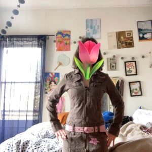 Brunt jeans jacka, low waist bälte - Brun jeans jacka med rosa bälte  Tyget känns som jeans, mangla mig inte om jag har fel 😘🤗 Low waist bälte  Man kan byta håll på bältet så det är samma färg som jackan  Jag tror det är hawaiianska hibiskusar på jackan Lite osäker på märket Fråga på! 🌷