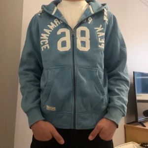 Peak performance zip up hoodie  - Ljusblå Peak performance zip up hoodie i storlek M. Den är i fint skick och ända defekterna är små färg fläckar på två ställen av tröjan och förstört snöre vid luvan. Tröjan passar även som storlek S.
