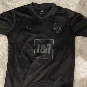 Dortmund fotbollströja  - Säljer denna feta borussia Dortmund all black limited edition 22/23 tröja med Bellingham#22 på ryggen. Perfekt inför sommaren. Jättebra skick, bara tryck vid storleken (se bild 3) som lossnat lite men inget som märks. Självklart äkta 🤝