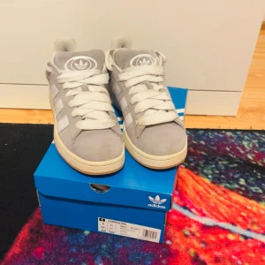 Grå Adidas Campus 00s - Adidas campus i färgen grå (Greh Three) med vita och gråa sko snören som ingår, kommer också med sko boxen. Andvända ett par gånger annars är de inga defekter på skorna. Strl 41 1/2 men passar 42 också! Ny pris 1 100kr (frakt ingår)💕