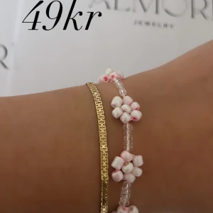 Två armband - Ett armband från Almori. Handgjort pärlarmband med vita och rosa pärlor formade som blommor.