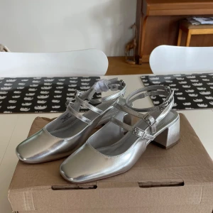 Silvriga Klackskor Mary Jane  - Silvriga klackskor från Asos i storlek 38. Det är Mary Jane stil med spännen vid anklar. Helt oanvända!  Slutsålda på Asos.