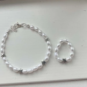 Egengjort pärlarmband och ring - Egengjort pärlarmband och ring gjorda på vita pärlor. Båda två har silver berlockersom avbildar stjärnor. 