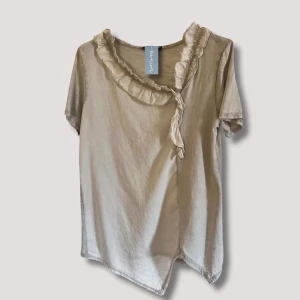 Dress Up Quick T-shirt - Söt bomulls T-shirt med volangkant längs halsen och framsidan. Något snedskuren i botten. Perfekt t-shirt att matcha med jeans för en avslappnad look eller klä upp med kavaj och dressad byxa.  One size, passar upp till st. 42  Material: 100% Bomull 