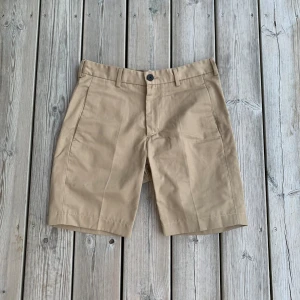 Chinoshorts från Elvine - Säljer ett par sköna shorts från Elvine i storlek 27. Har en bakficka med dragkedja och två sidfickor. Hör av dig vid frågor och funderingar!