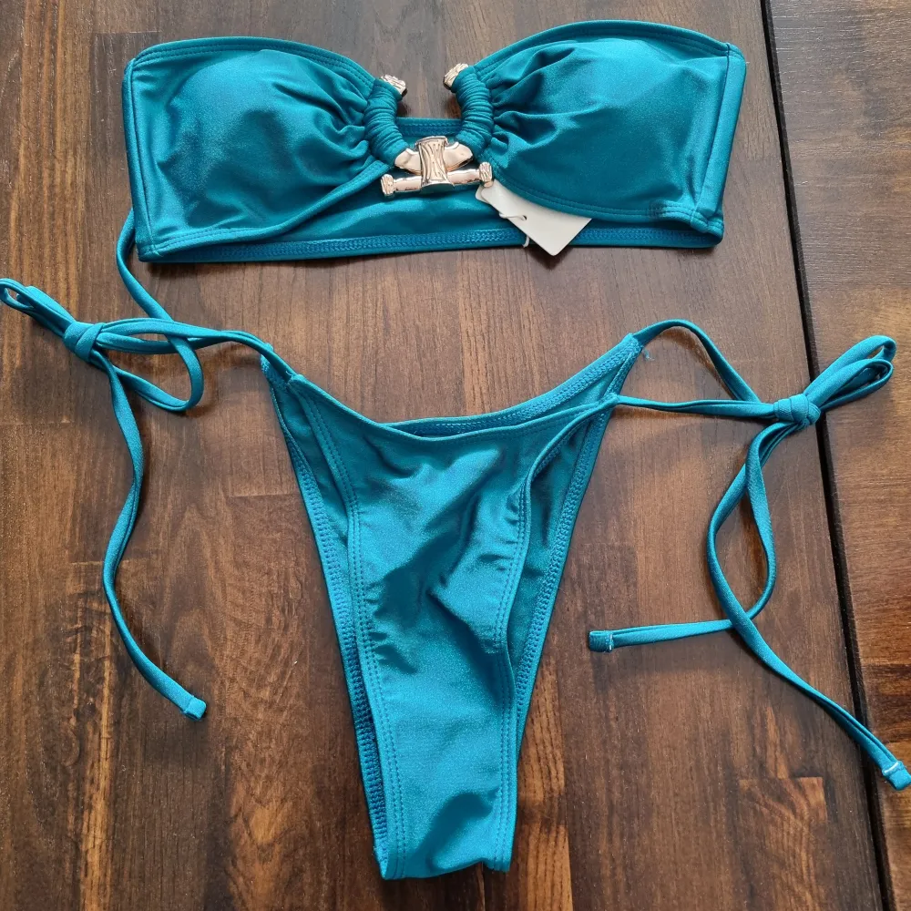 Helt ny bikini i skimrande petrol. Överdel i storlek S och underdel i storlek XS, dock justerbar i banden. Med lappar och trosskydd kvar.. Asusteet.
