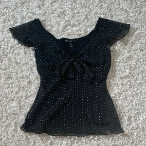 Prickig blus  - Säljer denna svarta blusen med knytning och vita prickar från H&M. Storlek 38. Köpt secondhand, men tyvärr har den inte kommit till användning av mig.