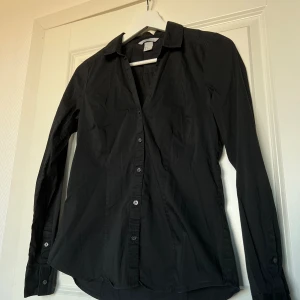Svart figurnära H&M skjorta - Fin, klassisk och figurnära svart H&M skjorta. I väldigt bra skick. Skönt och stretchigt material. Storlek 36, normal i storleken. Upphämtning i Malmö möjligt.