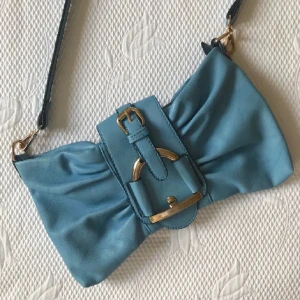 Blå axelremsväska - Säljer denna superfina axelremsväska!!💙💙 Ganska kort axelrem vilket gör att den sitter rätt högt upp vilket är supersnyggt! Rymlig innuti och har innerficka med dragkedja. Pyttelite slit som man ser på sista bilden men inget som stör 🥰🫶