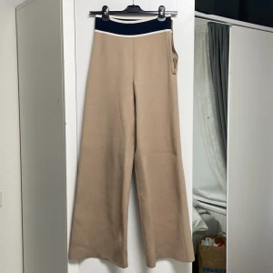 Utsvängda byxor med dragkedja - Utsvängda byxor med dragkedja i färgen beige, den är högmidjad. Nyskick endast använd en gång. Materialet är fint och bekvämt. Köpt för 299kr. 