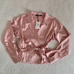 BikBok rosa omlottblus med rosett - Otroligt vacker blus från BikBok. Knyts som omlott med snöre på insidan och rosettband på utsidan. Ny med tags kvar. 