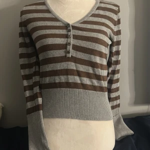 Brun/grå randig knitsweater  - En fin v-neck sweater med knappar. Har använts ett tal gånger, men är i hyfsat bra skick och har bra matrial. Skriv om mer information:) 
