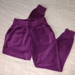 Lila/plommonfärgade mjukisbyxor/byxor i sammet, storlek XS/S. En lite kortare (nästan capri) modell med muddar nertill. 80% bomull 20% polyester. I bra använt skick (den undre sömmen runt resåret i midjan har delvis lossnat, men det gör inget). 