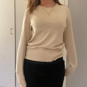 Krämvit topp  - En långärmad tröja med guld knapar på handlederna. 