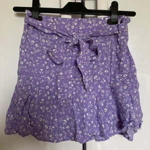 Lila vit blommig rosett knyta bälte kort kjol skort sommarkläder shorts - Stängs med dragkedja i sidan. Har ”shorts” under kjolen.