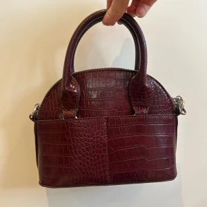 Liten väska! - Söt vinröd väska från Zara. Aldrig använd och inga synliga defekter. Har ett långt axelband som går att ta av. Köpt för flera år sedan. 