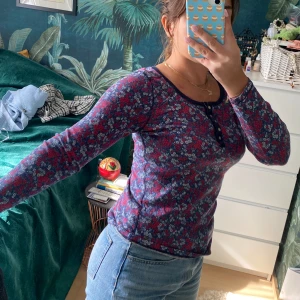 Mönstrad långärmad tröja  - En så söt långärmad tröja med mönster i blått och rött. Knappar i fram som går att knäppa upp.  Ribbad i tyget, väldigt skön och stretchig.  Lite längre i bak än vad den är i fram.