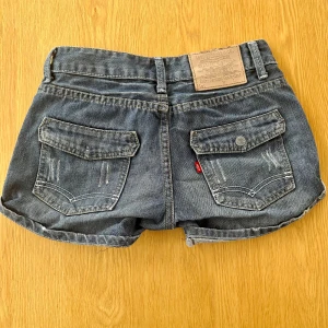 Lågmidjade Levis shorts  - Lågmidjade shorts från Levis, storlek saknas med passar mig som vanligtvis bär XS/32 och gissar på att de kan va 24/25 i midjan. Knappen på en ficka har gått av men annars är de i bra skick 💕skriv för bilder på mig och mått 🌸🌸
