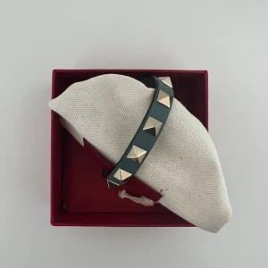 Valentino armband  - Valentinoarmband i grön blå färg. Super fint skick, enda defekten är att det blivit lite slitet vid spännet. Se bild 3. Finns extra nitar. Armbandet användes mer flitigt för 4 år sedan och har inte blivit används sen dess. Därav fortfarande bra skick