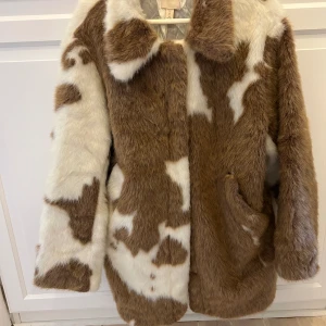 Pälsjacka i ko mönster - Jacka i fint skick i ko mönster! Fickan sitter inte fast på ena sidan, men ingenting som stört mig. Därav lågt pris. 