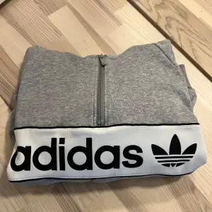 Grå hoodie från Adidas. Detaljer på ärmarna samt två fickor framtill med dragkedja.  Lite mindre i storleken xs/s